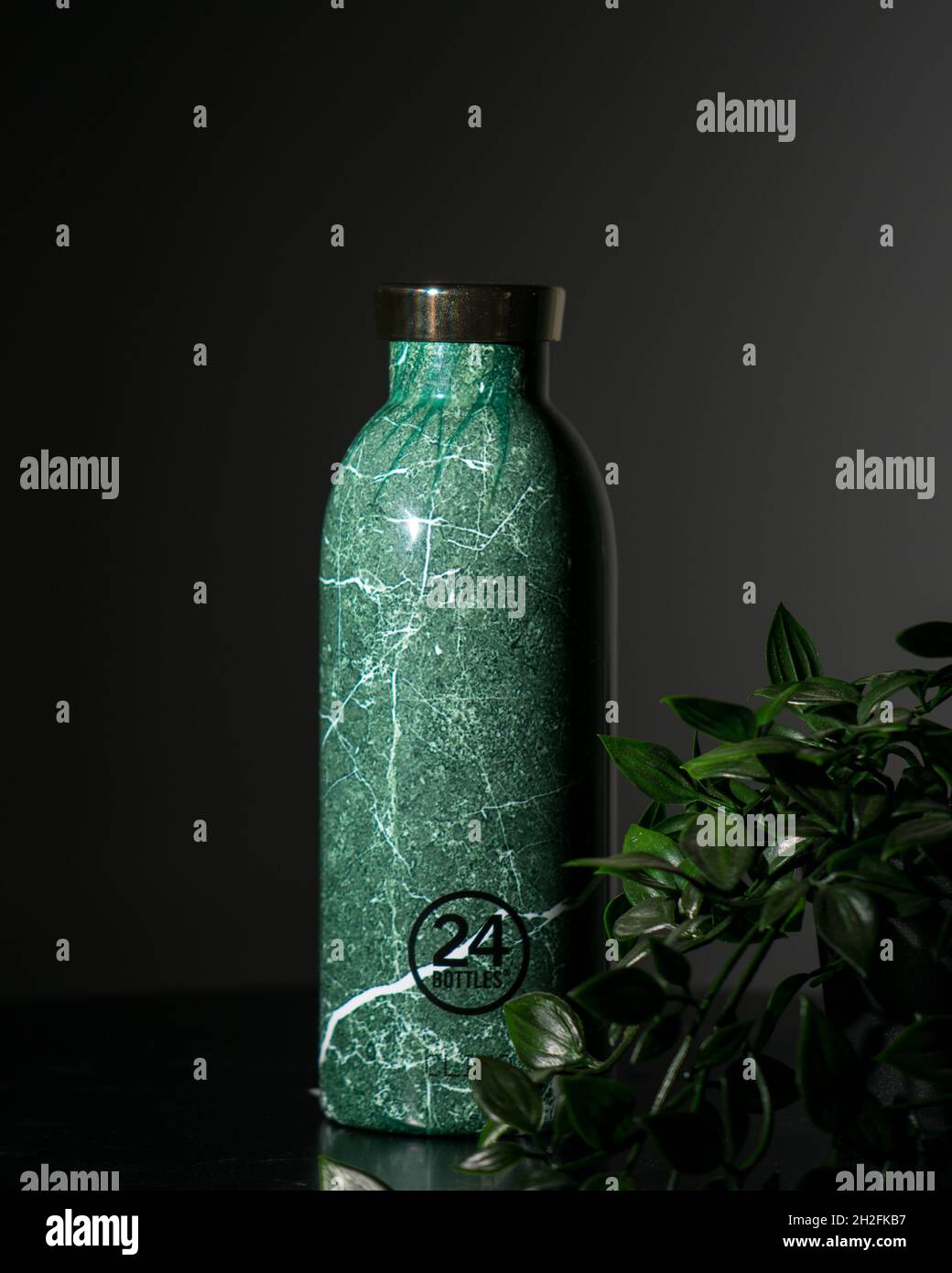 NICOSIA, CYPRUS - Jun 21, 2021: An image of a green marble stainless steel reusable water bottle and decorative plant leaves on a table Stock Photo