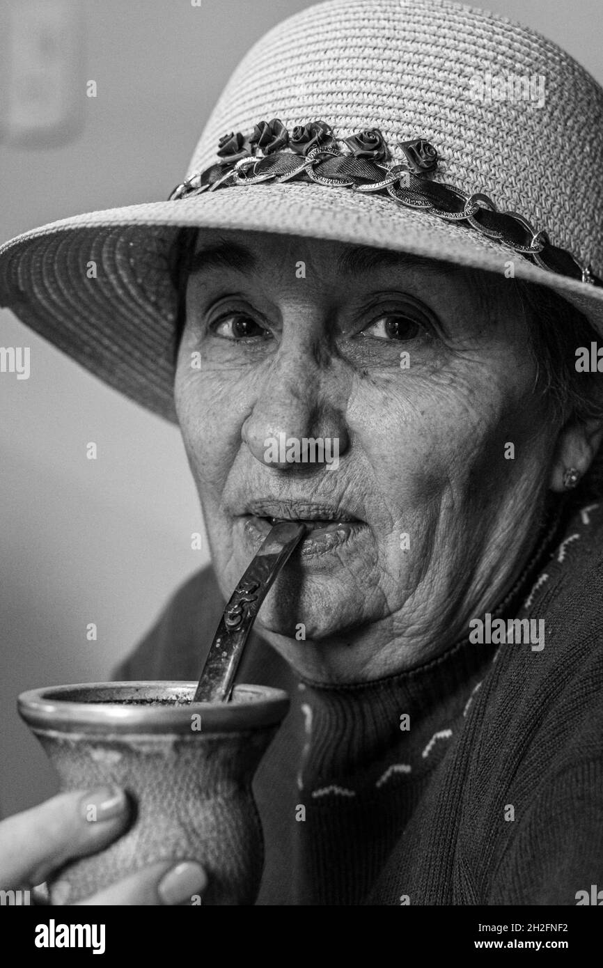 Grayscale shot of an old Hispanic woman with a toquilla straw hat drinking from a clay cup Stock Photo