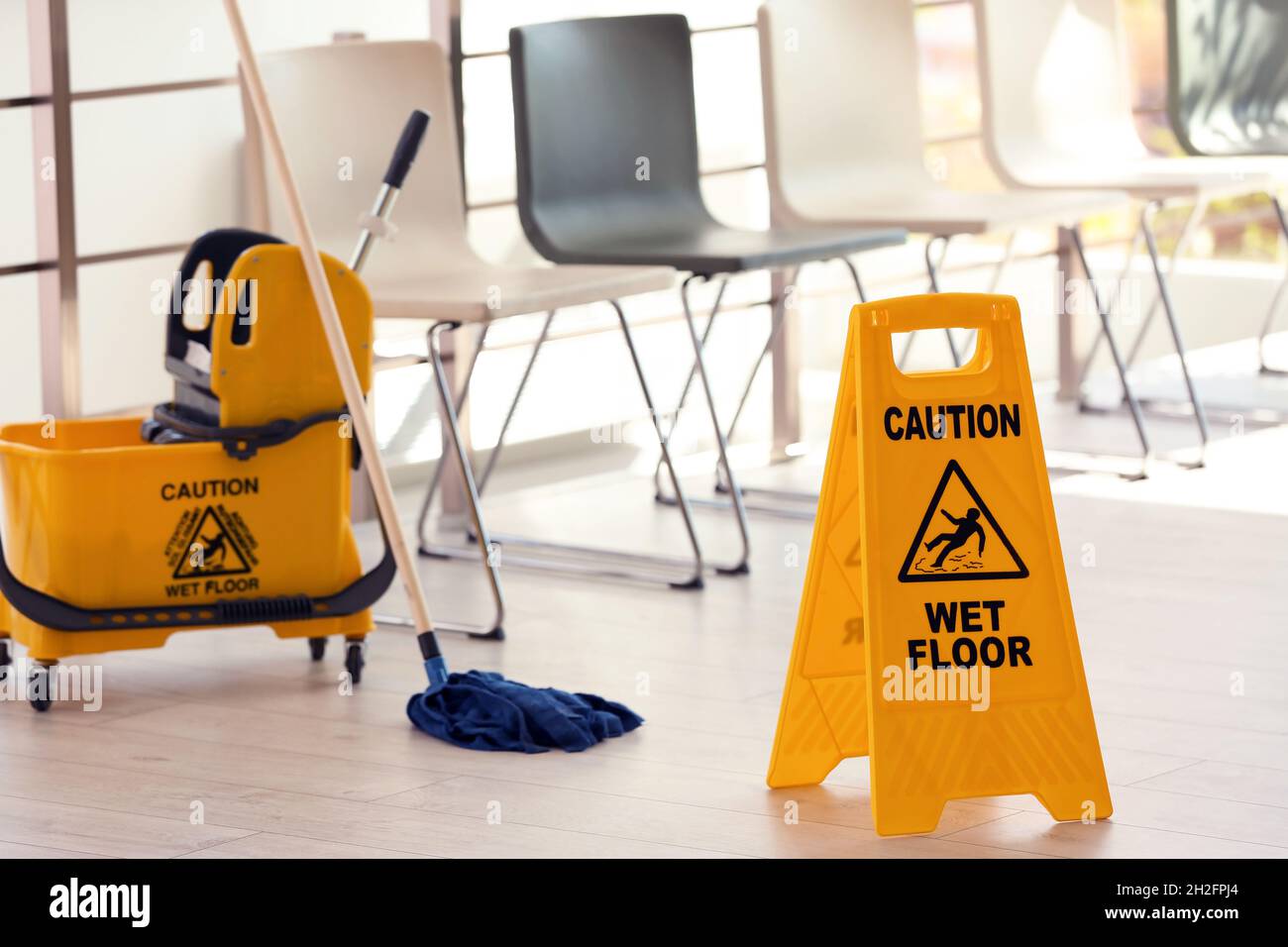 Safety sign with phrase Caution wet floor and mop bucket, indoors