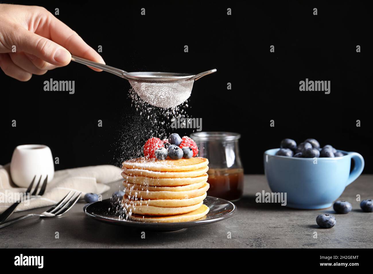 Woman adding sugar powder to tasty pancakes with berries on plate, closeup Stock Photo