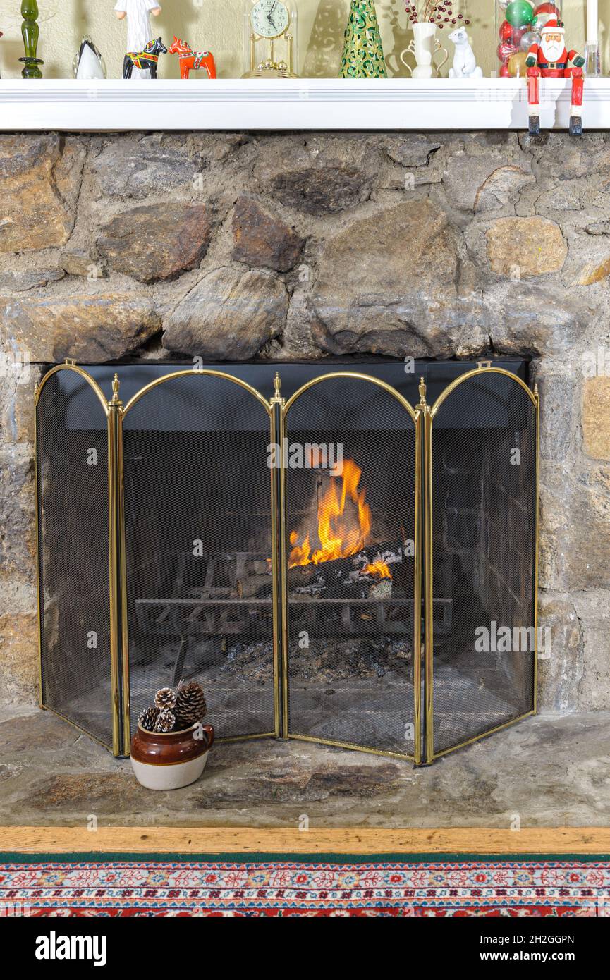 Fire iit in a cosy fieldstone fireplace decorated for the Christmas holidays Stock Photo