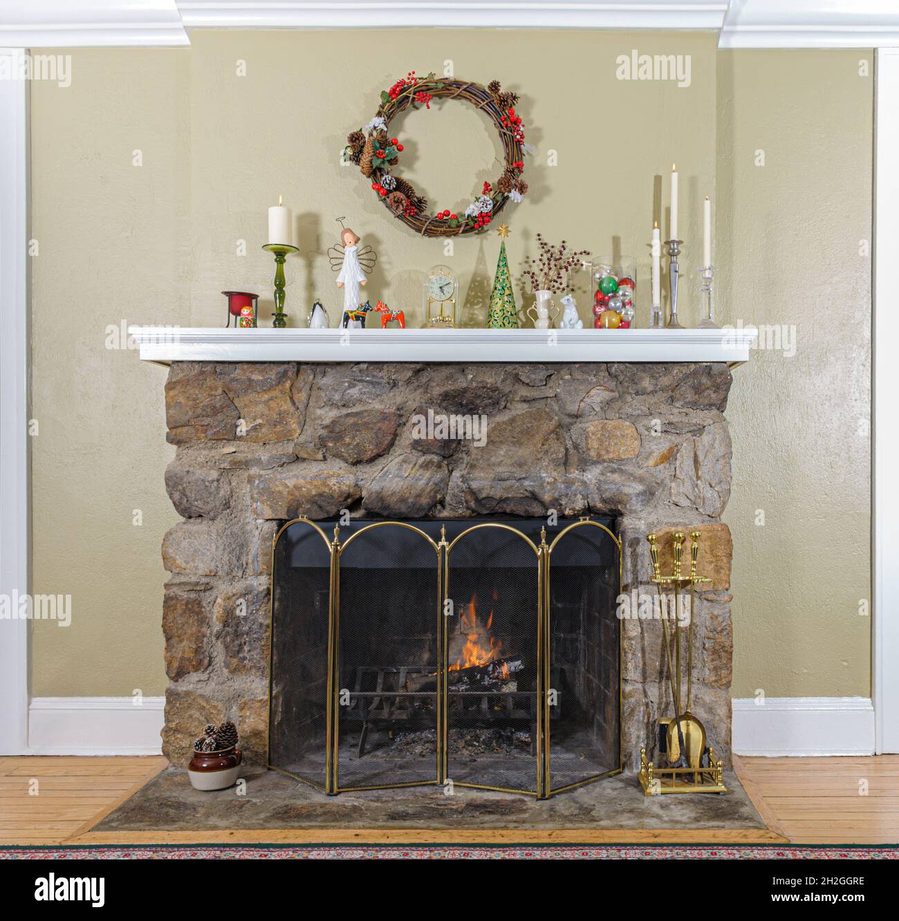 Rustic stone wood burning fireplace with a cosy fire and mantlepiece with Christmas decorations and a holiday wreath. Stock Photo