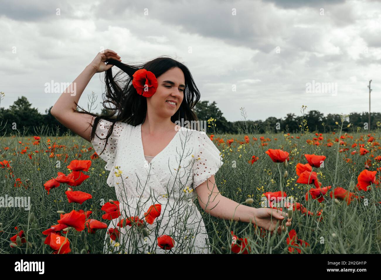 Beautiful young woman wearing white dress, standing in poppy field Stock Photo