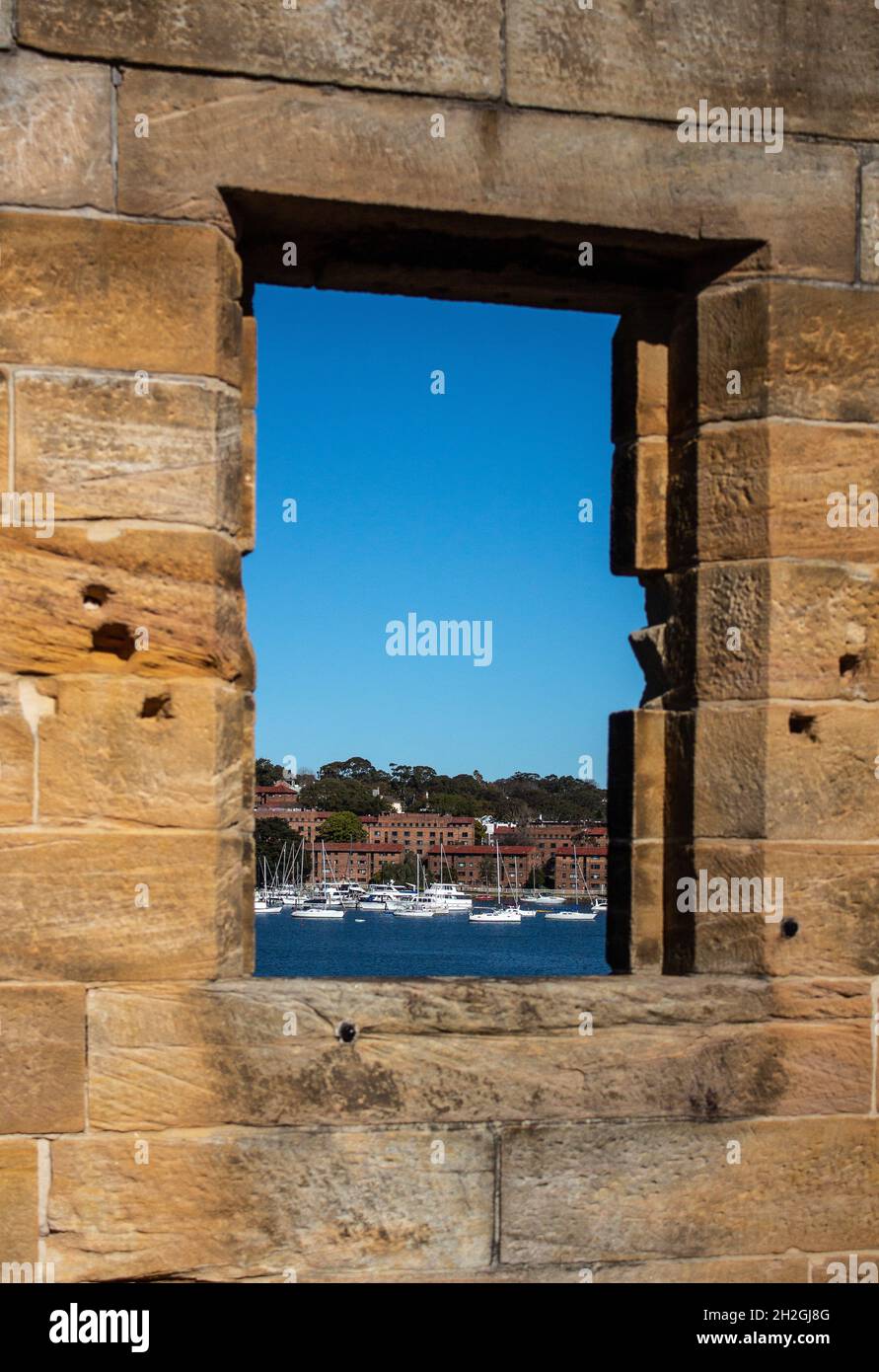 Sandstone brick wall with open window showing boats on water against blue sky Stock Photo