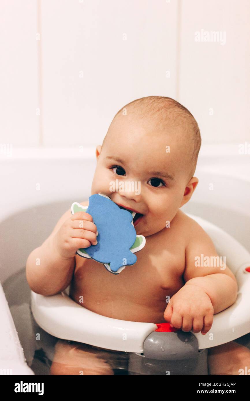 Sweet funny baby taking a bath. Baby chewing a toy in a bath chair