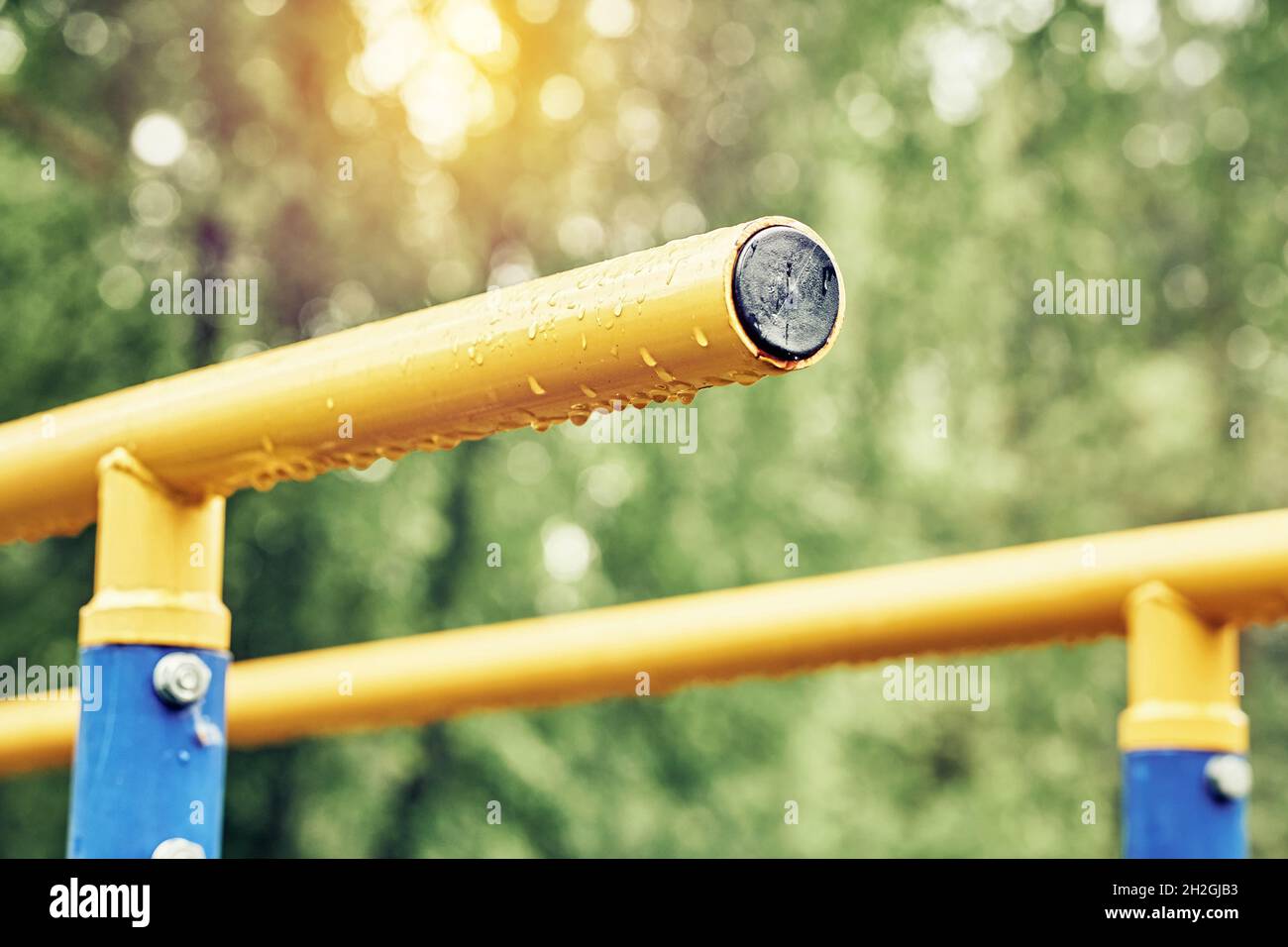 Yellow metal bars for exercises with hanging rain drops at sports ground in spring green park on cloudy day extreme close view Stock Photo