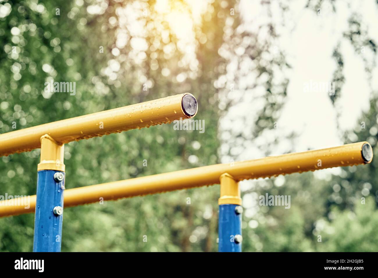 Yellow metal bars for exercises with hanging rain drops at sports ground in spring green park on cloudy day extreme close view Stock Photo