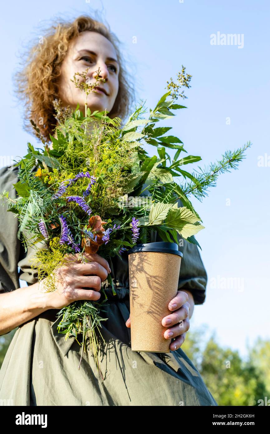 Young beautiful woman in a green summer dress holds a bouquet of wildflowers. Positive blonde middle-aged model. Summer season. Sunlight. Rest and rel Stock Photo