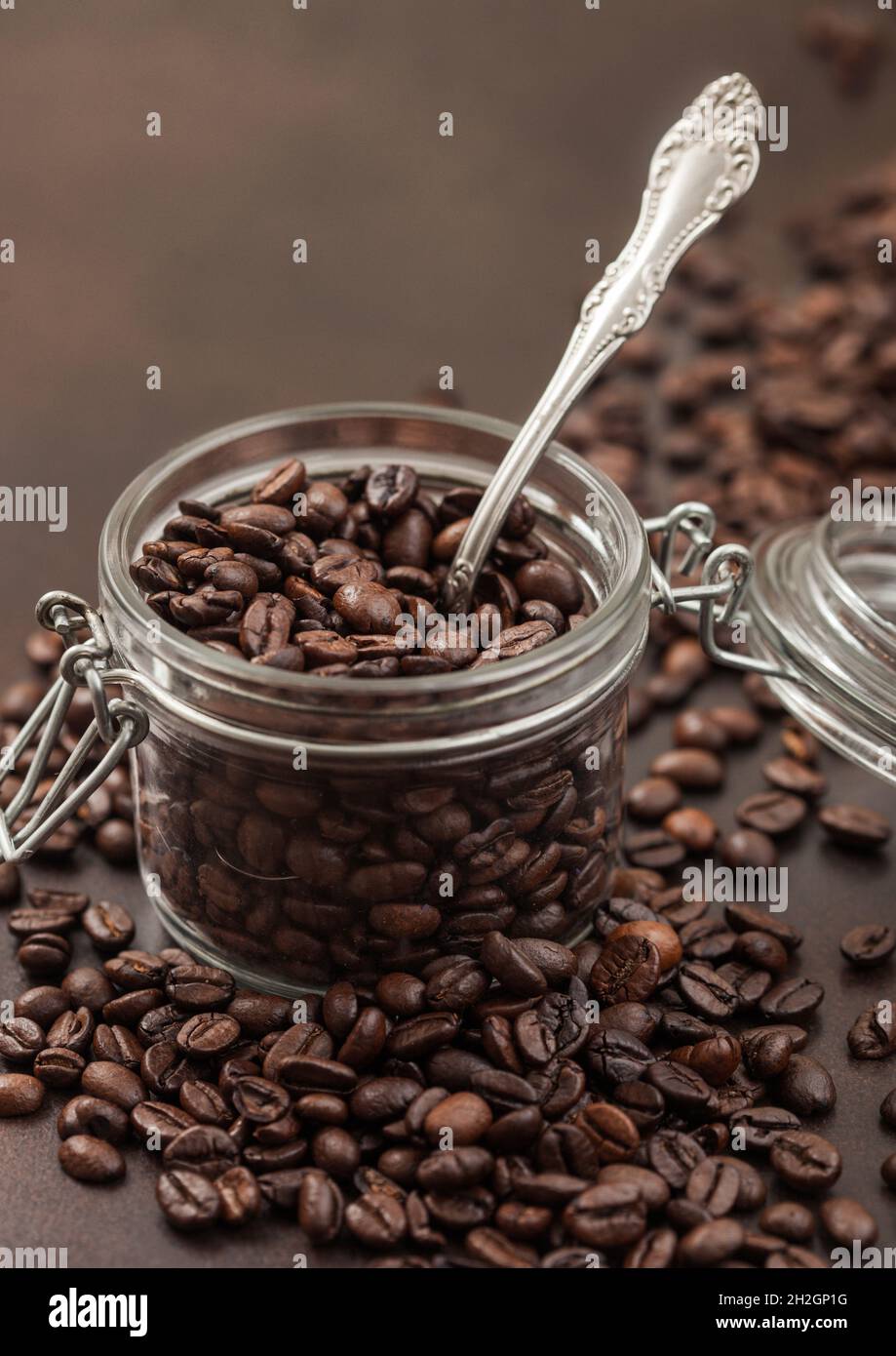 Roasted coffee beans in glass jar with steel spoon on brown background
