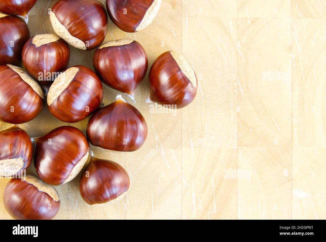 Flat-lay background image of fresh, raw sweet chestnuts on a wooden chopping board Stock Photo