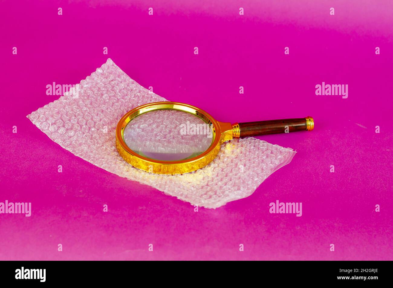 Magnifying glass and bubble wrap on pink background. Selective Focus. Stock Photo