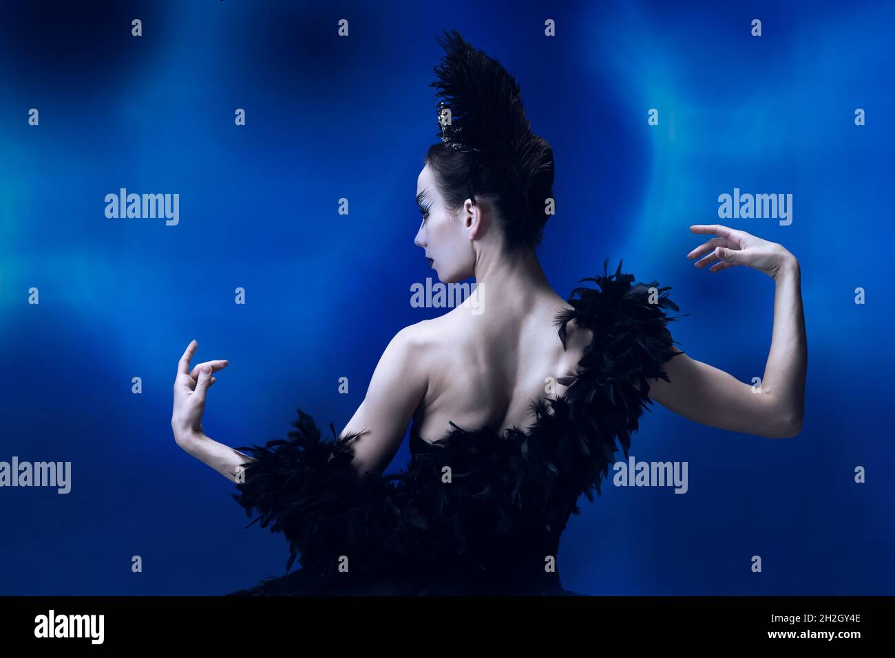 Back view of beautiful woman, flexible ballerina in black ballet outfit, tutu dancing at blue studio full of light. Stock Photo