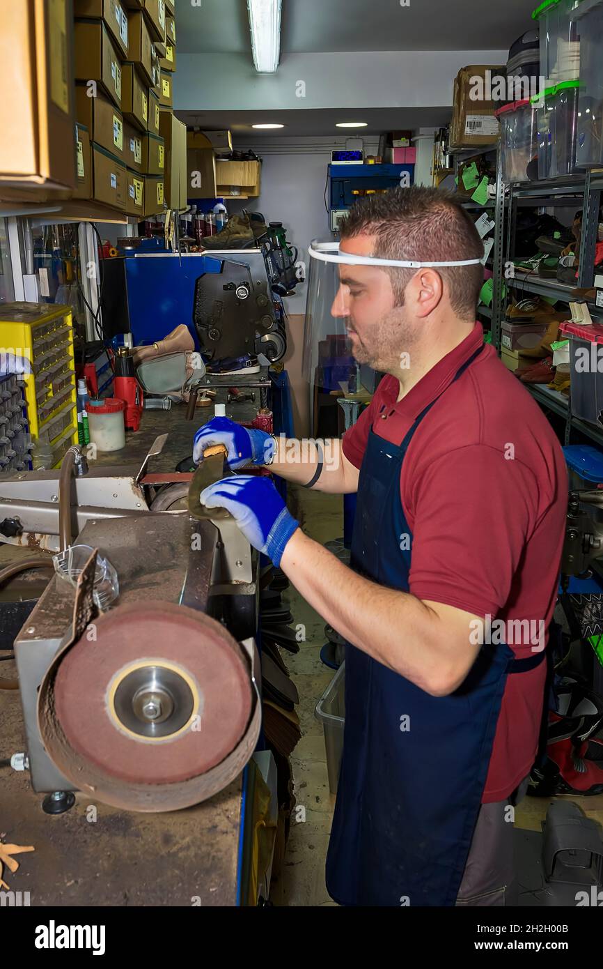 Young shoemaker mending footwear in repair shop. Stock Photo