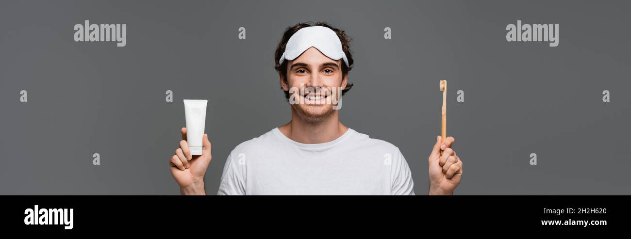 Smiling man in sleep mask holding toothbrush and toothpaste isolated on ...