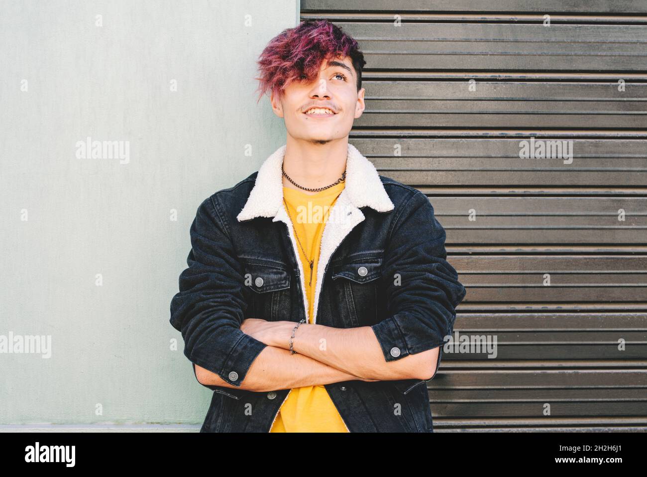 Stylish handsome teenage boy in denim jacket with burgundy hair color and  arms crossed looking up and smiling. Happy stylish teenage boy daydreaming  w Stock Photo - Alamy