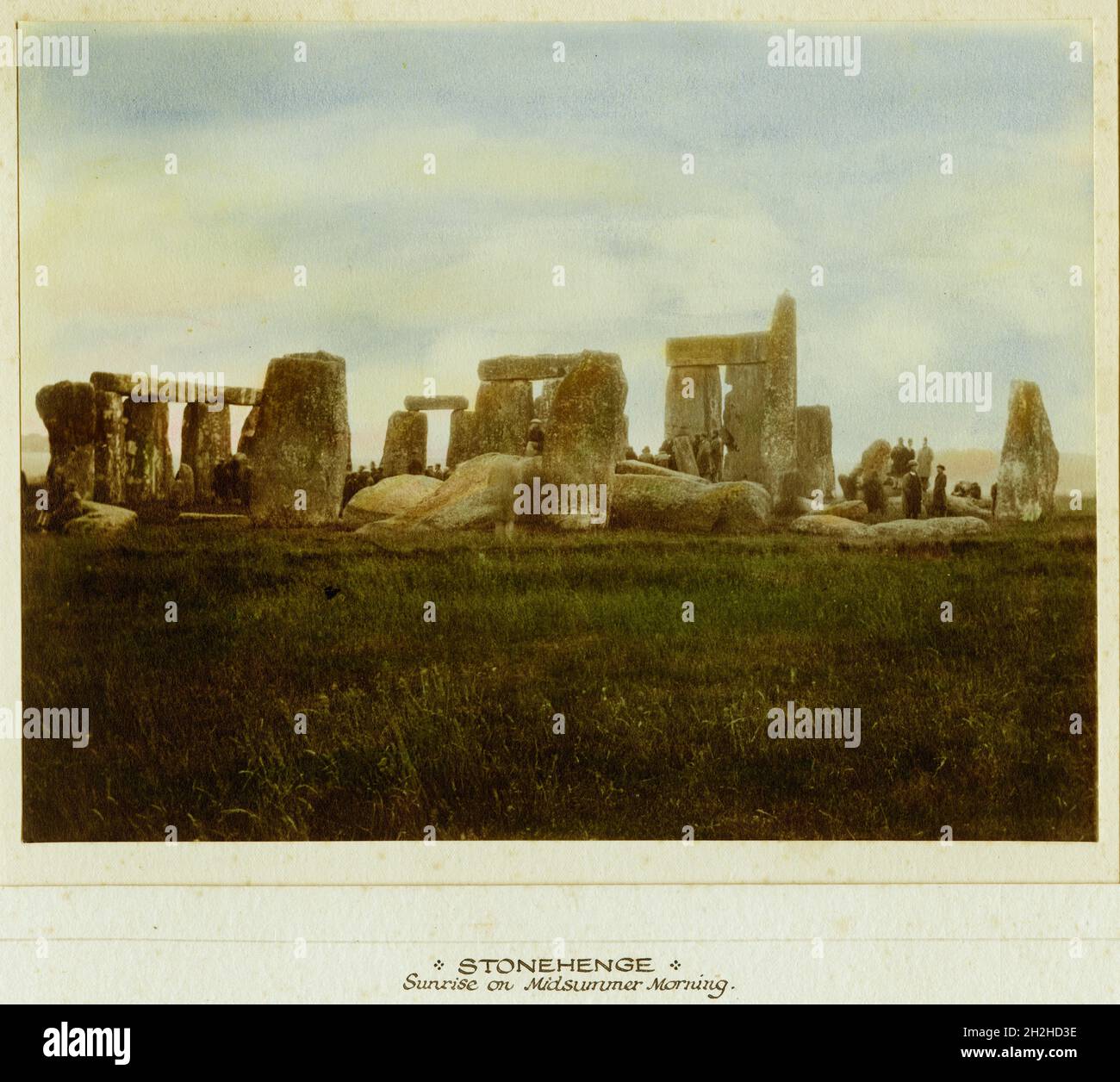 Stonehenge, Stonehenge Down, Amesbury, Wiltshire, 1925-1935. Mounted hand coloured print of Stonehenge titled, 'Sunrise on Midsummer Morning', showing figures around the henge monument. Stock Photo