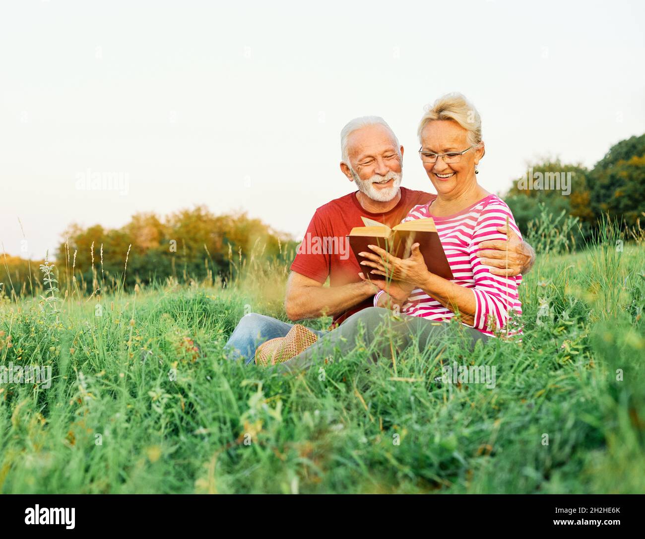 woman man outdoor senior couple happy lifestyle retirement together smiling love reading nature book Stock Photo