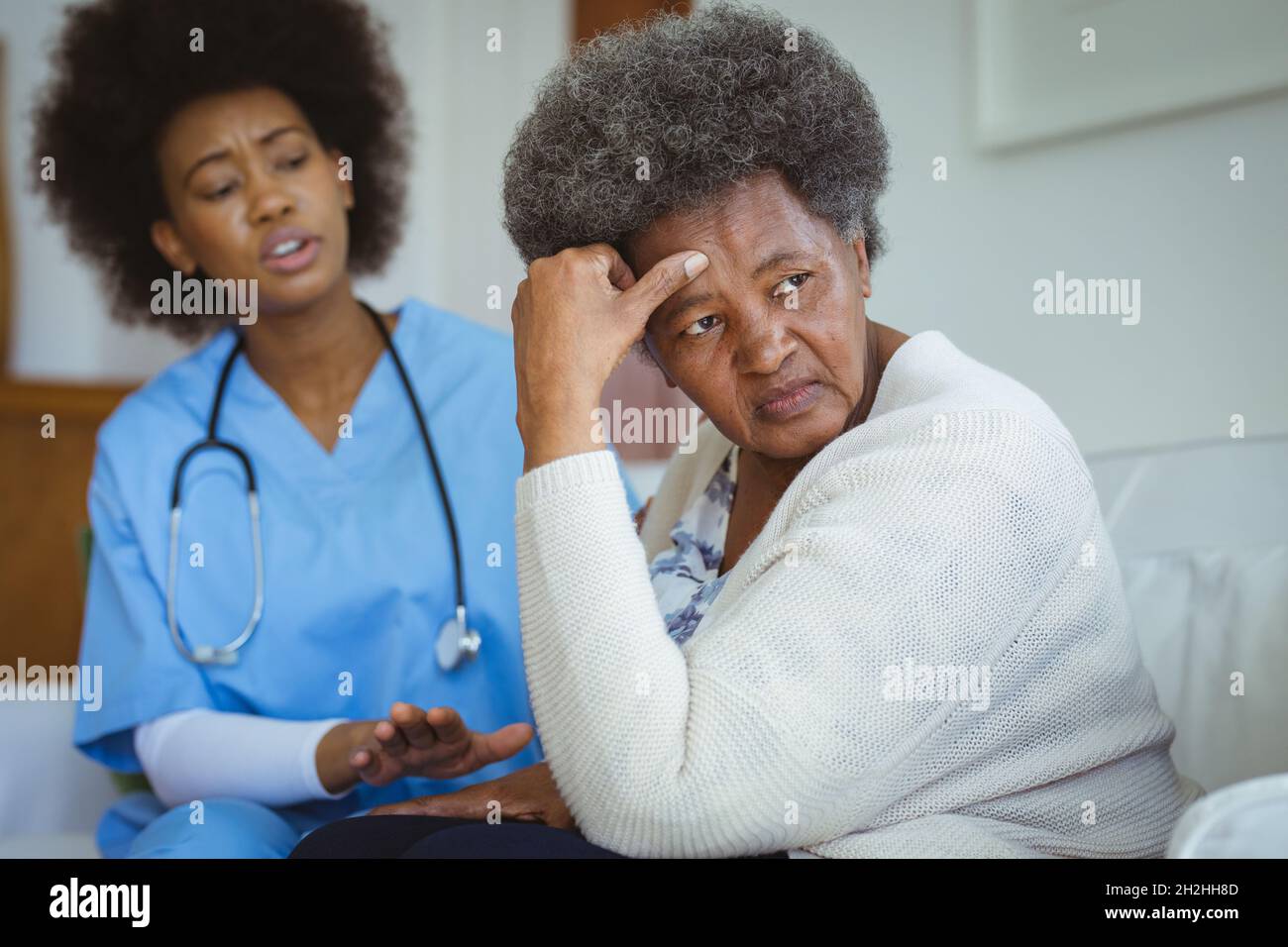 African american female doctor talking with sad senior female patient at home Stock Photo