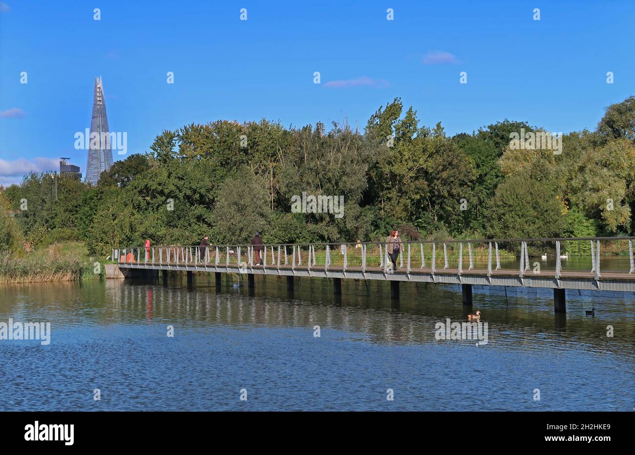Footbridge across the lake in Burgess Park, a large public green space in the heart of Southwark, London, UK. Shows The Shard on the skyline. Stock Photo