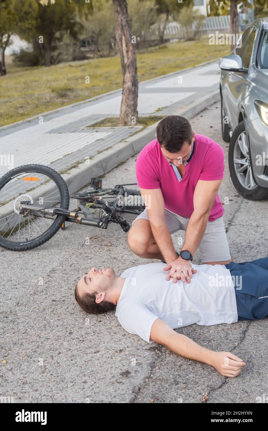 A man performs cardiopulmonary massage CPR on a young man who was run over while riding his bike. Bicycle accident with a car without wearing a helmet Stock Photo