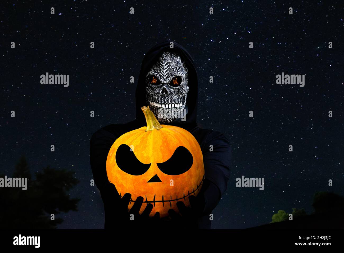 Grim reaper holding halloween pumpkin head. Man in death mask with fire flame in eyes on night sky starry background. Halloween holiday concept. Dark Stock Photo