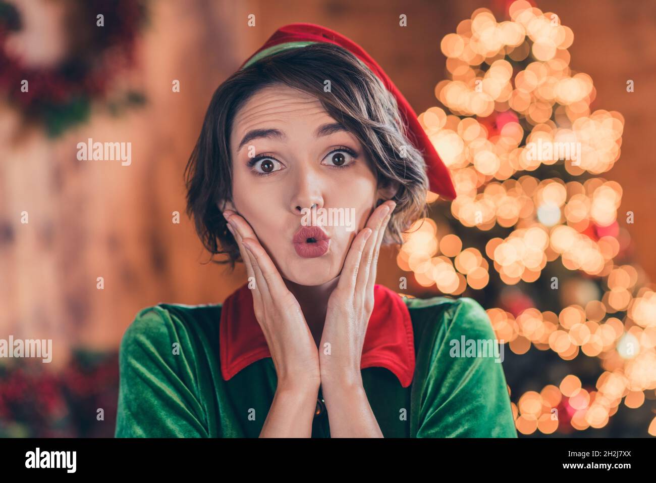 Photo of impressed cute young lady wear elf clothes celebrating christmas arms cheeks indoors house home room Stock Photo