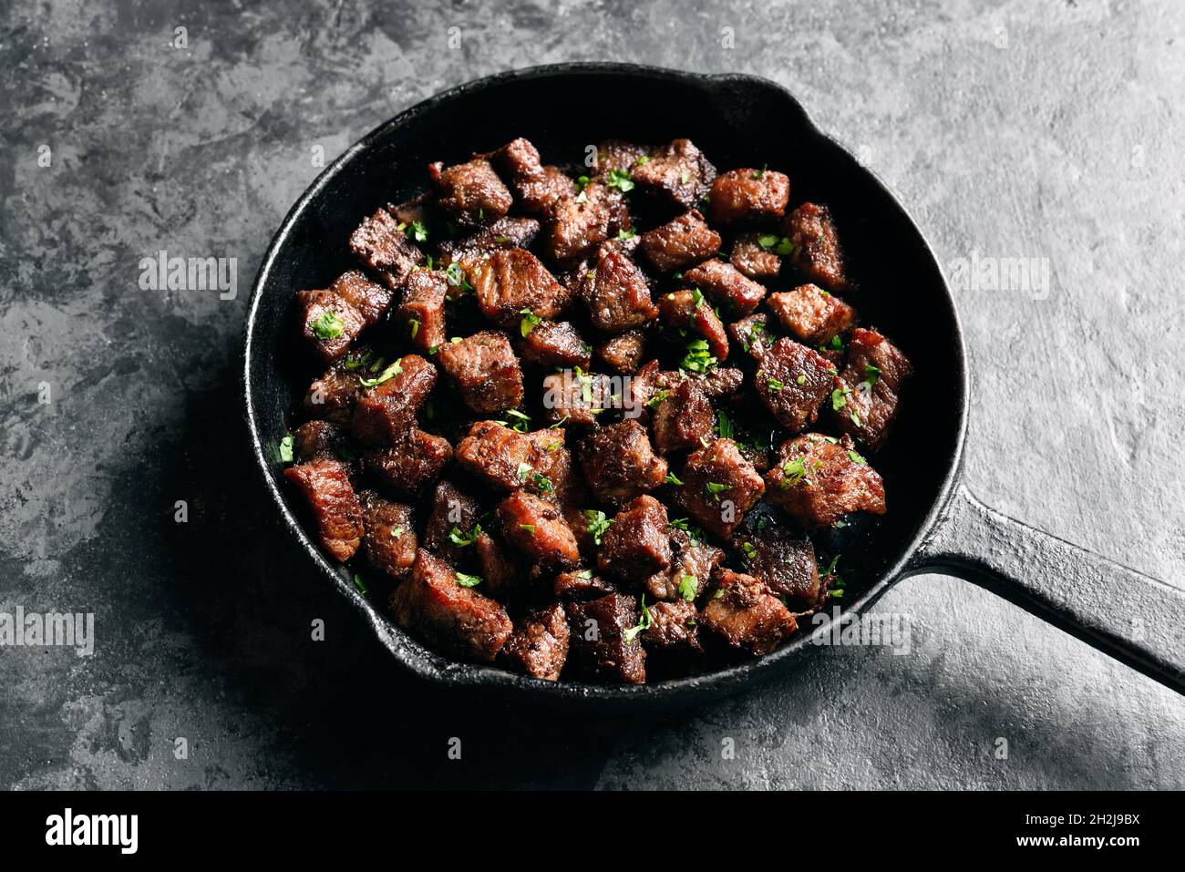 Close up view of garlic butter steak bites in cast iron pan over dark