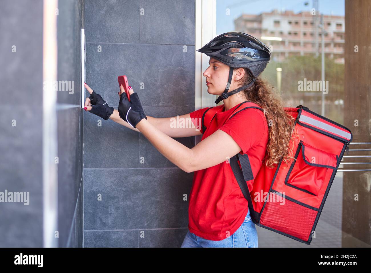 A cyclist delivery girl ringing the intercom bell Stock Photo