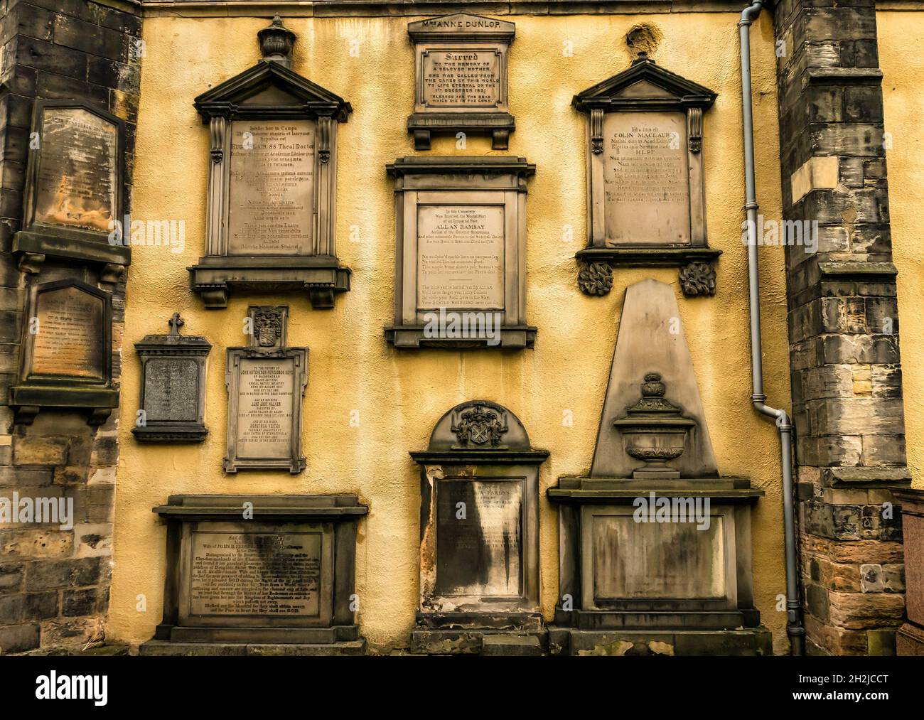 Yellow wall of Greyfriar's Kirk, Edinburgh, Scotland, UK lined with historic ornate carved commemorative tombs and headstones Stock Photo