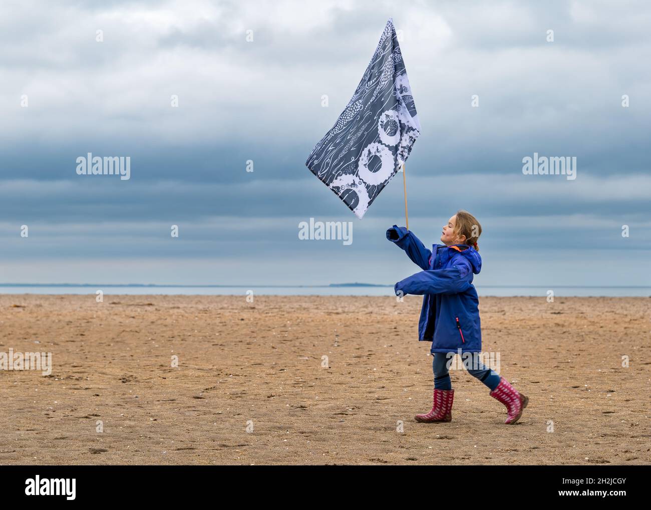 Child carrying flag walking across beach in Cop26 Pilgrimage, Belhaven Bay, East Lothian, Scotland, UK Stock Photo