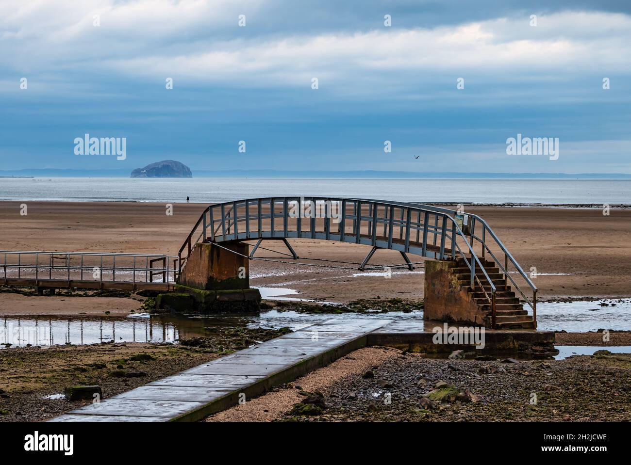 View of Bass Rock across Firth of Forth in moody weather & Bridge to Nowhere footbridge, Belhaven Bay, East Lothian, Scotland, UK Stock Photo