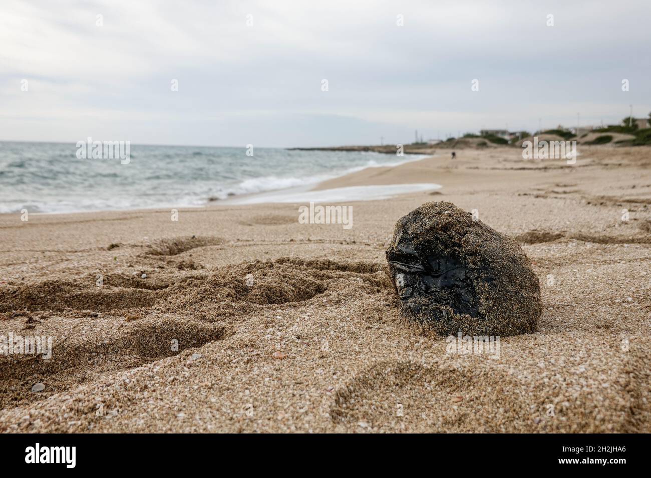 A block of black tar on the beach. Residue from hydrocarbon processing. There is a huge ecological problem in the Mediterranean sea. Stock Photo