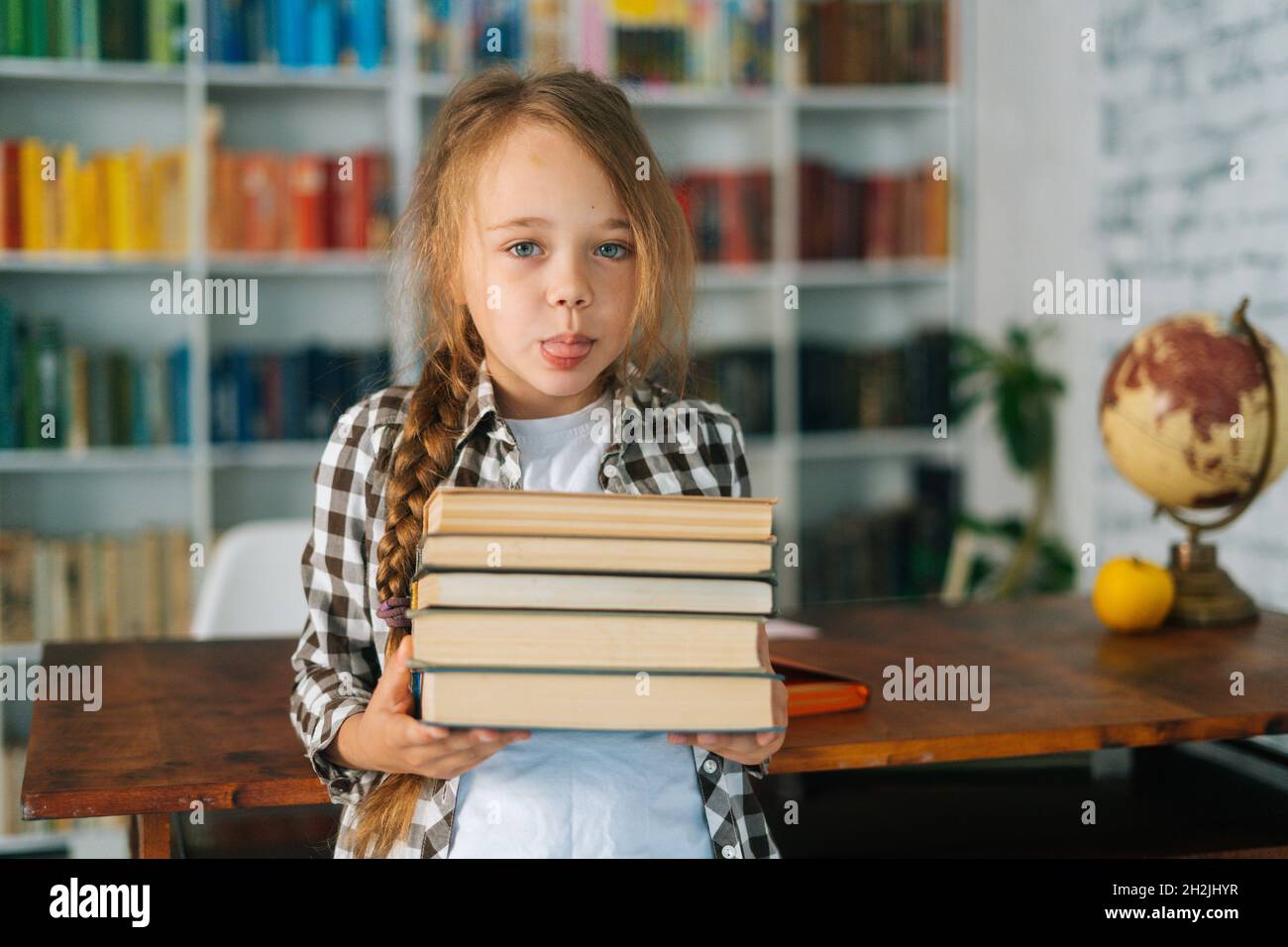 Portrait of playful elementary child school girl holding stack of books ...