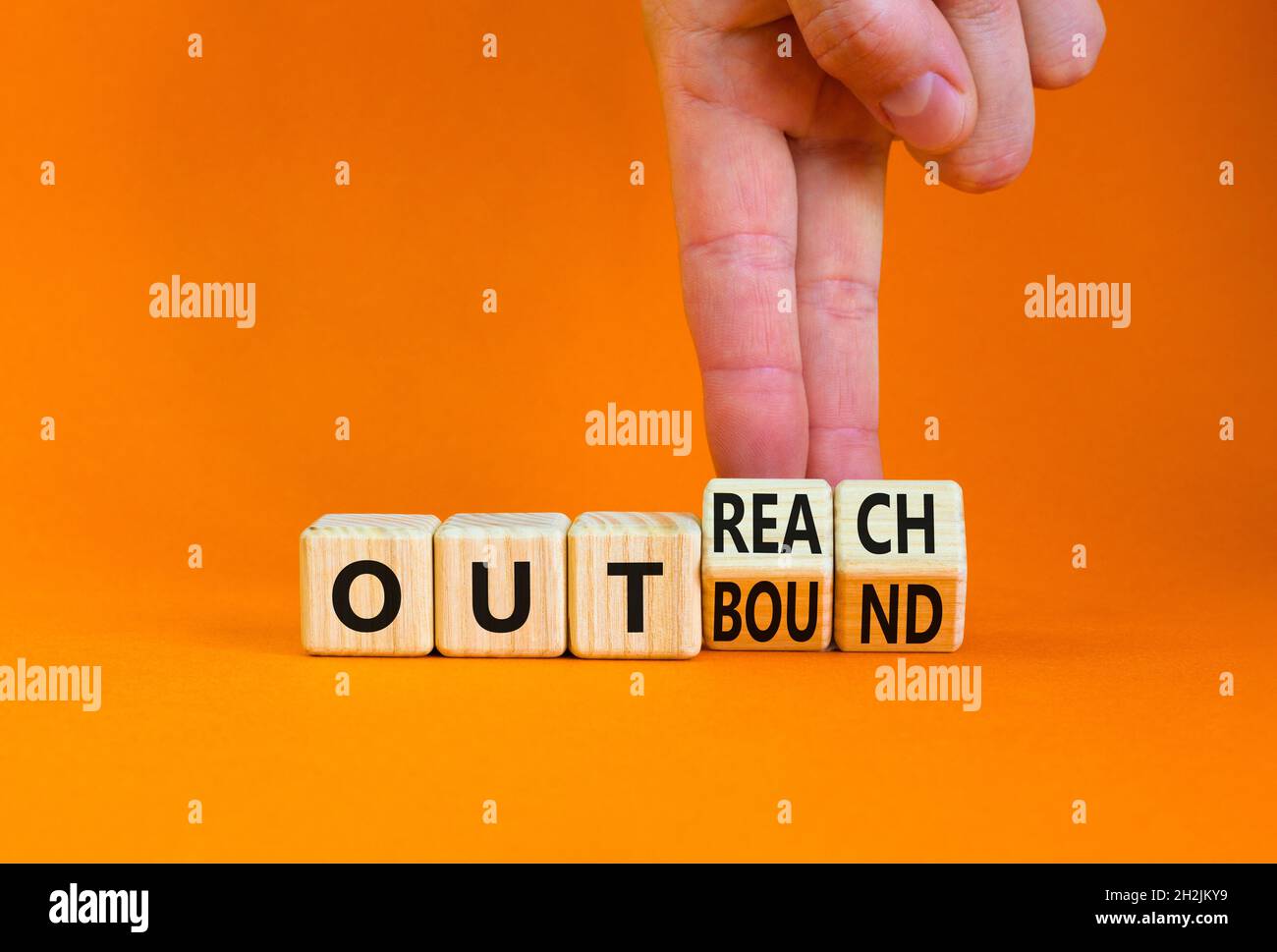 Outreach or outbound symbol. Businessman turns wooden cubes and changes the word 'outbound' to 'outreach'. Beautiful orange table orange background. B Stock Photo