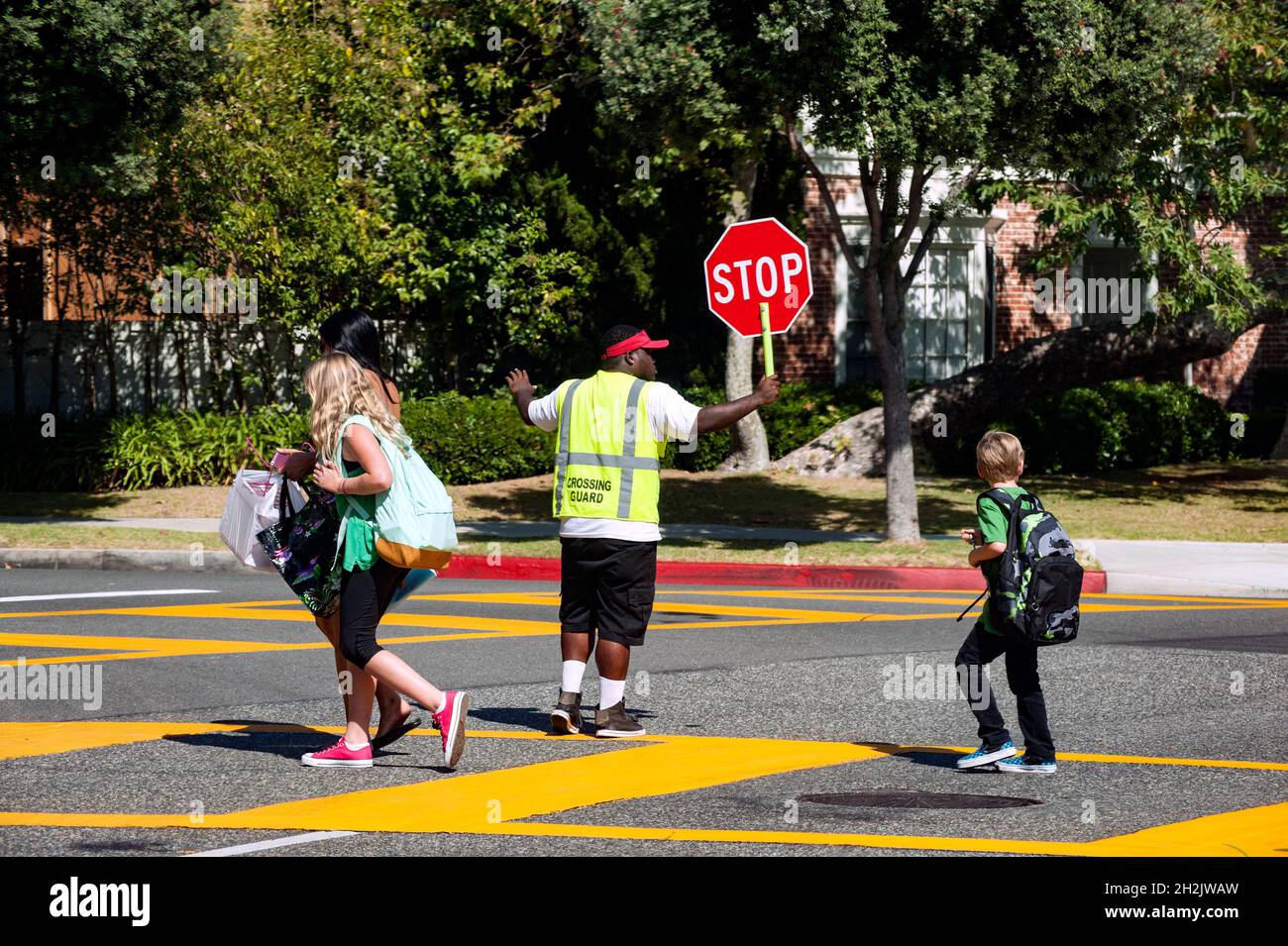 School children crossing a busy street with the aid of a crossing guard Stock Photo
