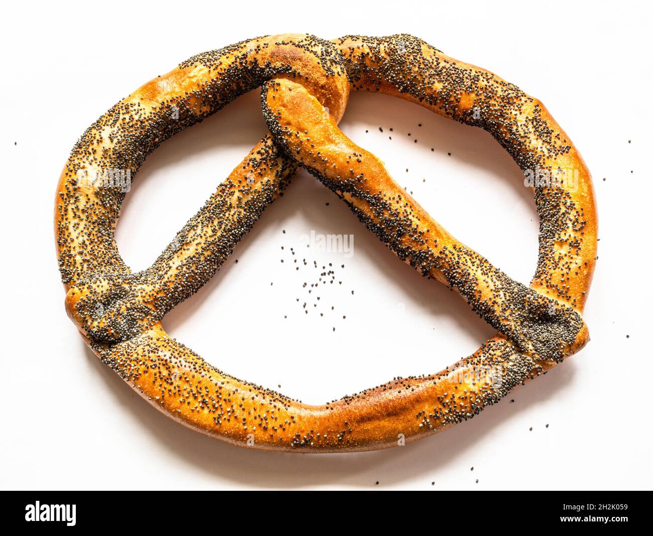 single pretzel sprinkled with poppy seeds on white paper background Stock Photo