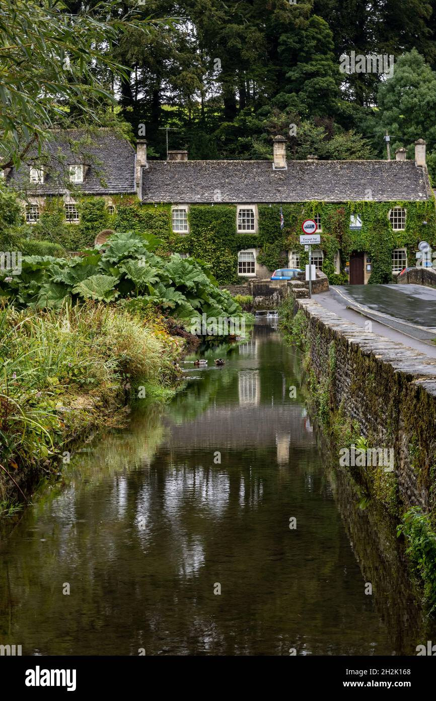 The stone bridge over the River Coln and the ivy covered Swan Hotel in the picturesque village of Bibury in the Gloucestershire Cotswolds, England. Stock Photo