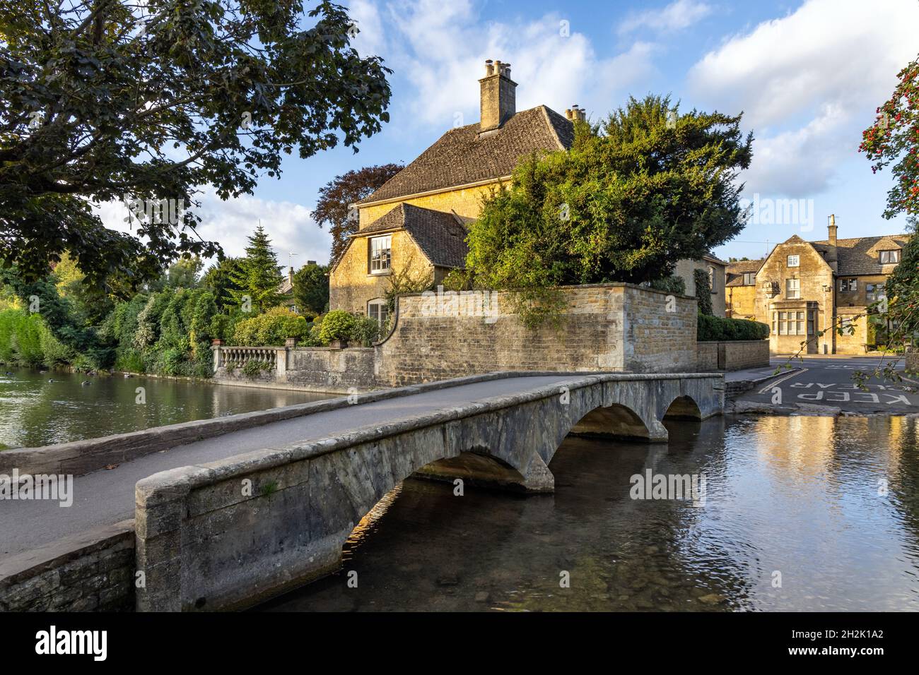 An arched stone bridge crossing the River Windrush in the picturesque Cotswolds Village of Bourton-on-the-Water, Gloucestershire, England. Stock Photo