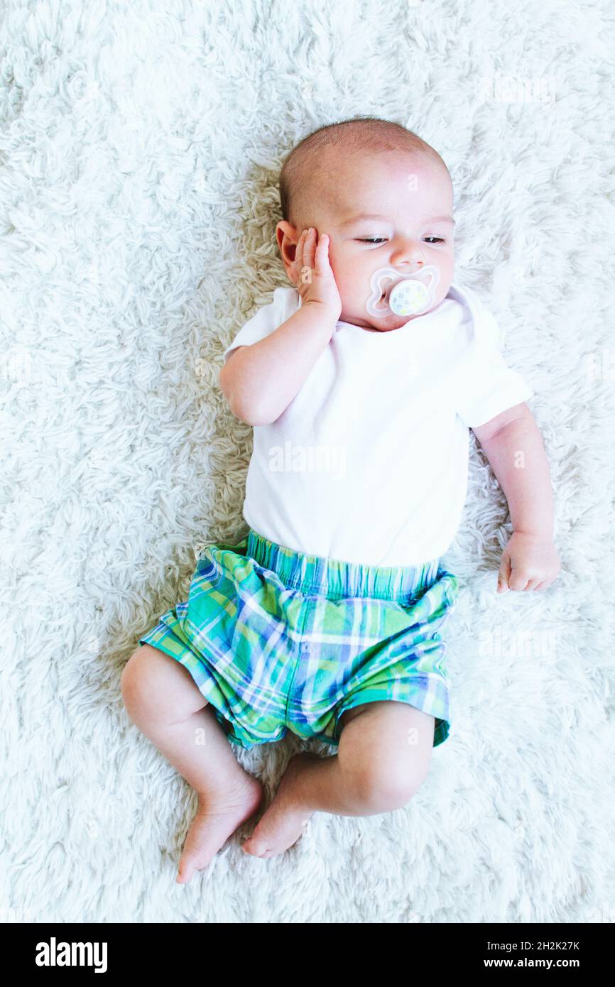 A baby with a pacifier holding his hand by his ear Stock Photo