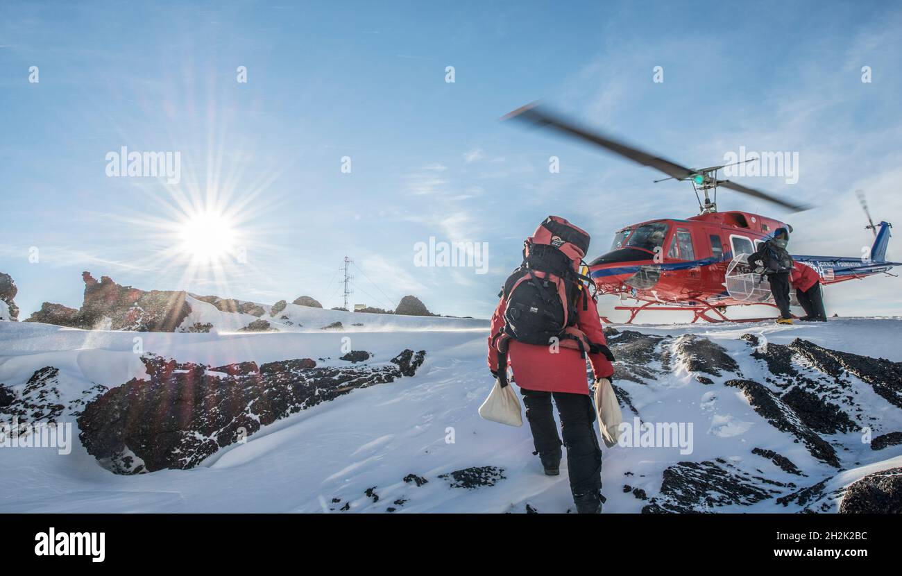 A scientist carries samples to a helicopter on a volcano in Antarctica Stock Photo