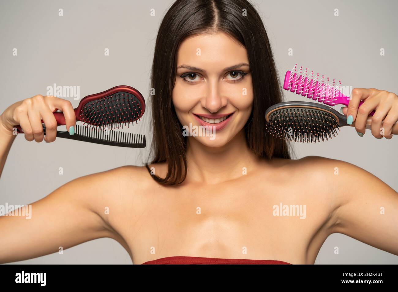Young woman with long hair posing with hairbrush and comb on a gray