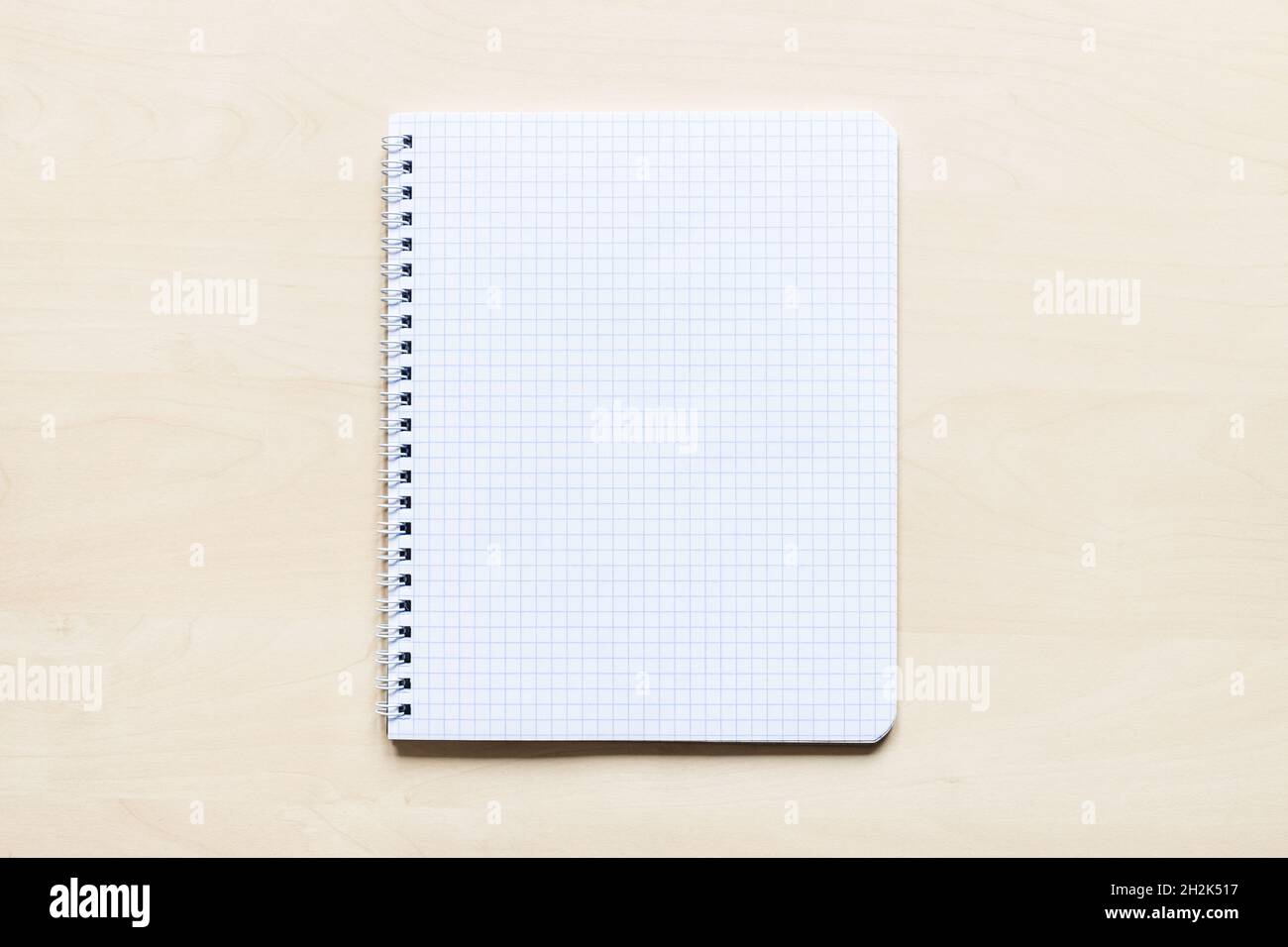 top view of blank sheet of squared paper of spiral notebook on light brown wooden board Stock Photo