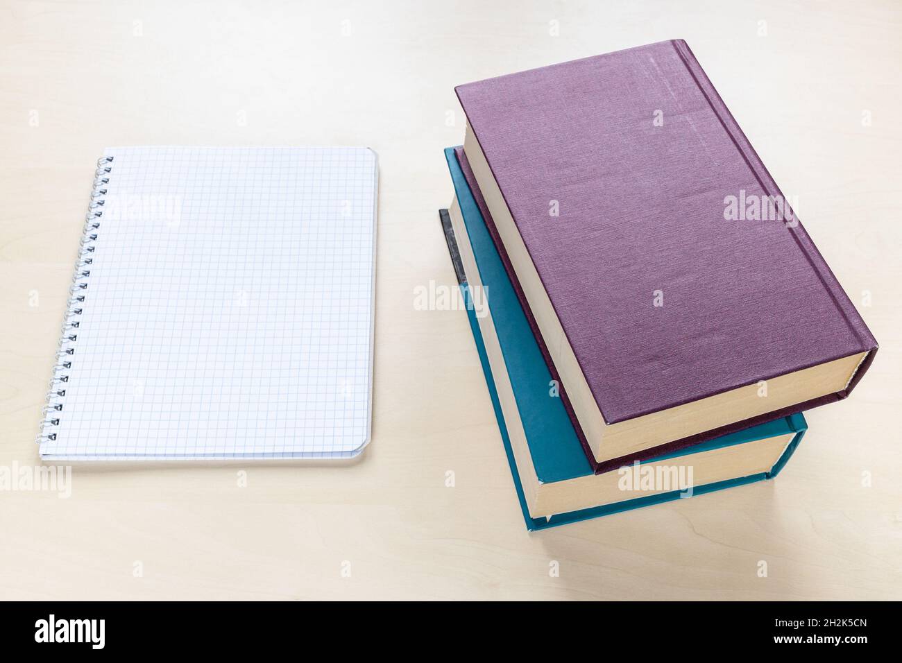 above view of two thick books and blank spiral notebook with squared paper on light brown wooden board Stock Photo