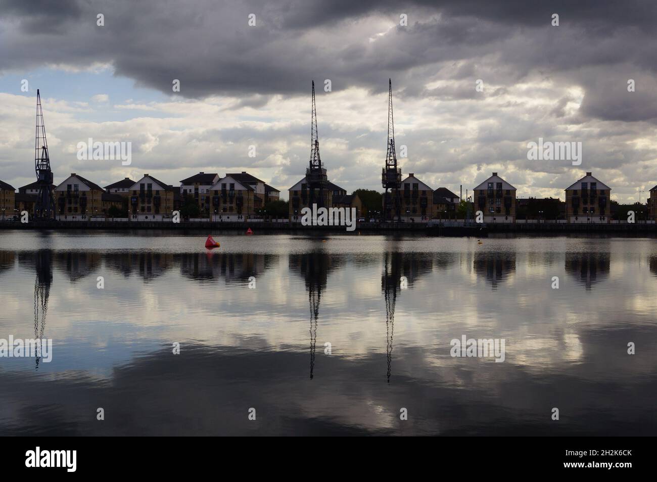 Cranes and houses reflecting in the water at London Royal Docks in east London (UK) Stock Photo