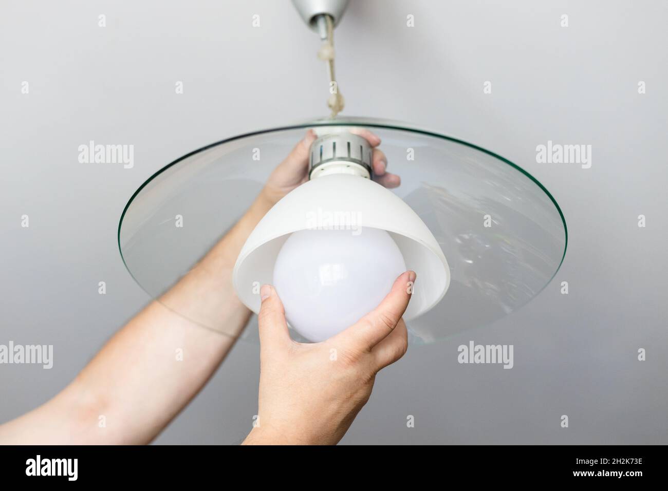 man replaces bulb of ceiling lamp at home Stock Photo