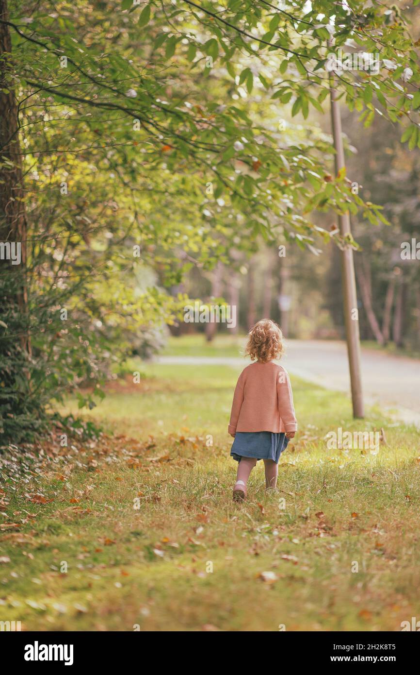 A Caucasian little girl with a pink jacket and a blue skirt walking in ...
