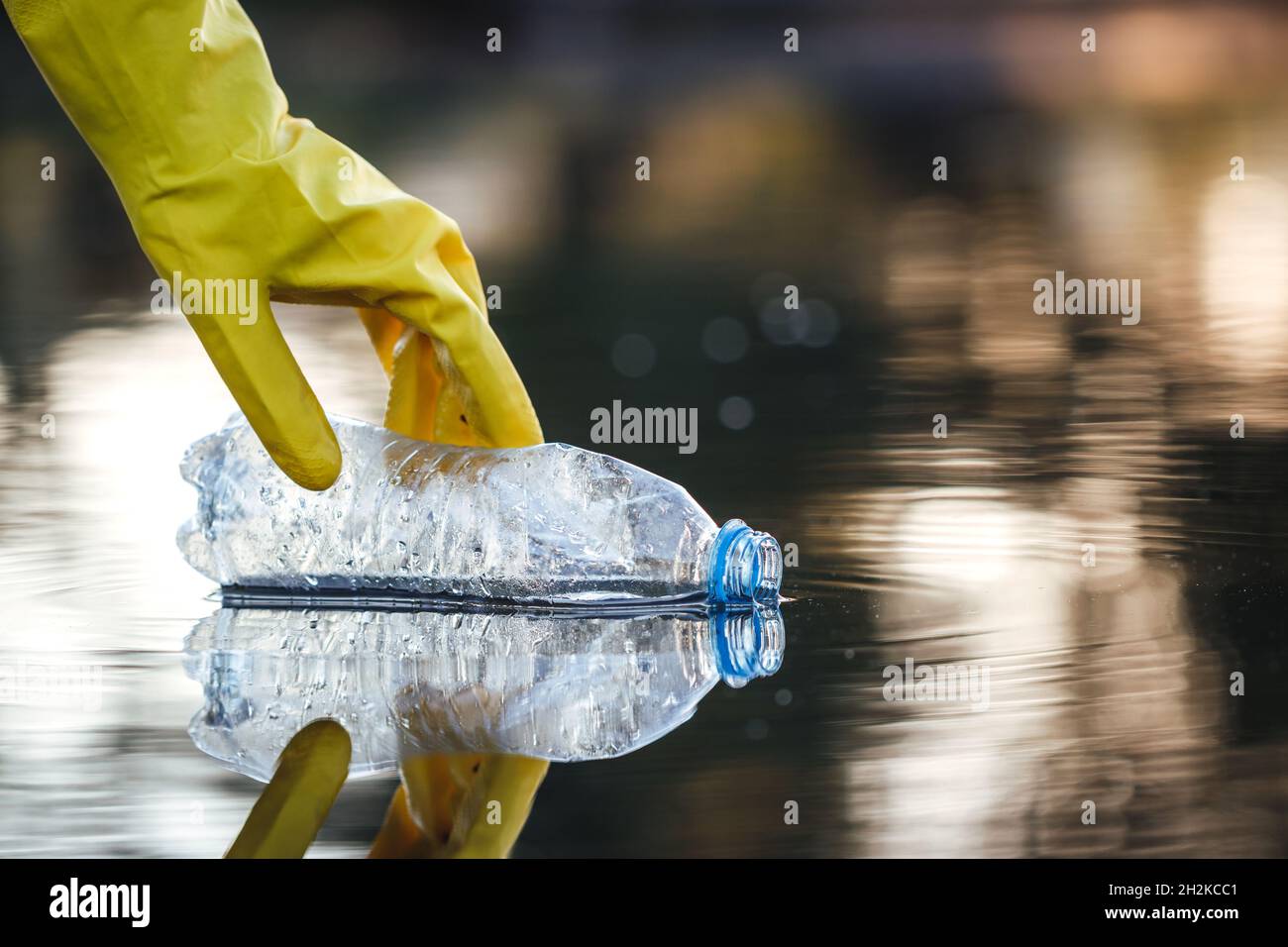Hand with protective glove picking up plastic bottle from polluted