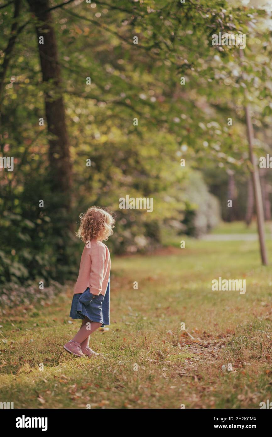 A Caucasian little girl with a pink jacket and a blue skirt in the park ...