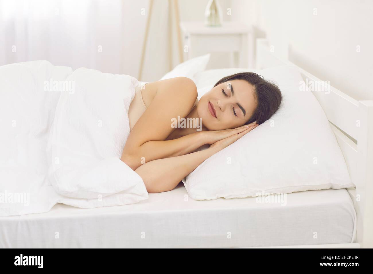 Beautiful woman enjoying good night's sleep on white sheets and pillow in her bed Stock Photo