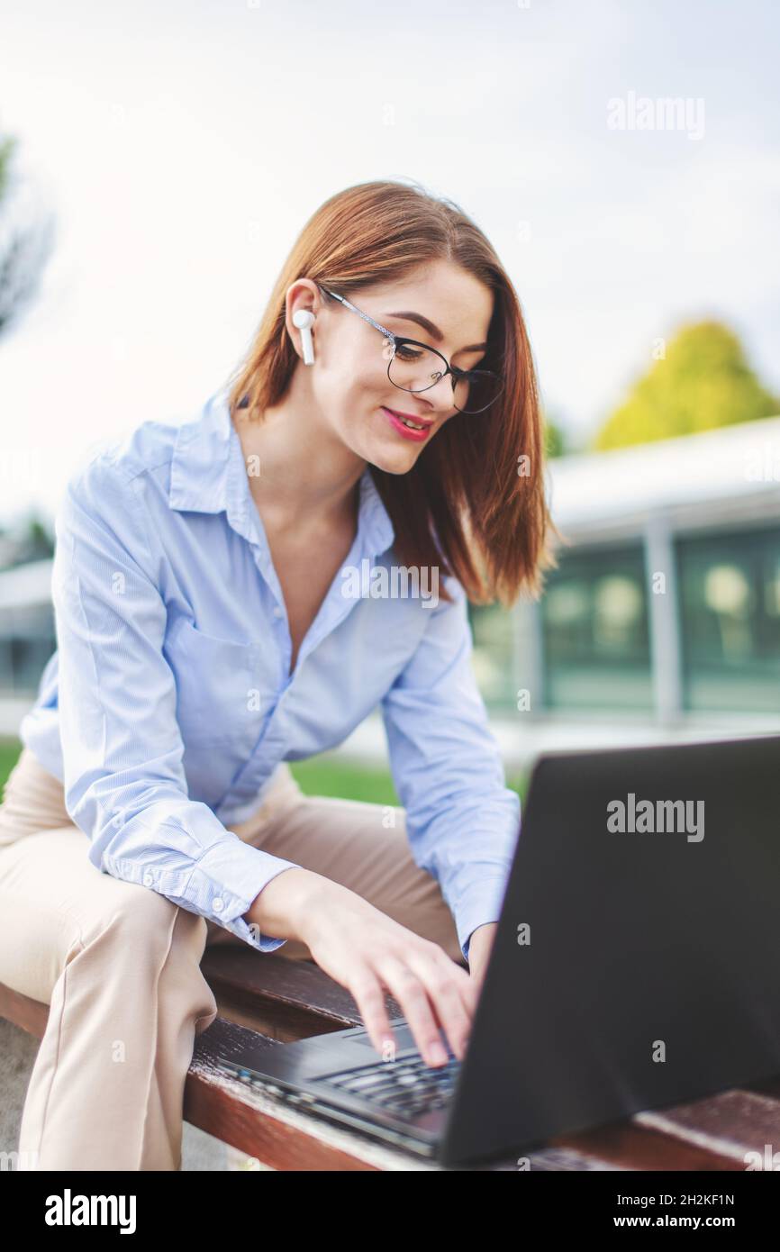 Young redhead woman online communicating in park by laptop and hands free headset Stock Photo